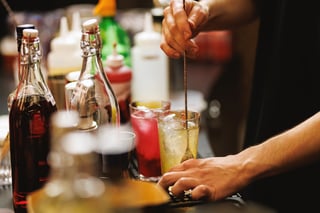 Close-up view of a bartender's hands stirring a drink in a glass surrounded by bottles and bar equipment.