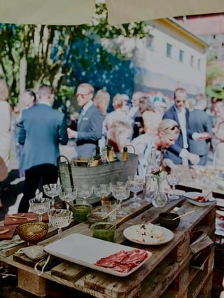 Havefest med gæster i festlig tøj omkring dekorerede borde med vin og charcuterie